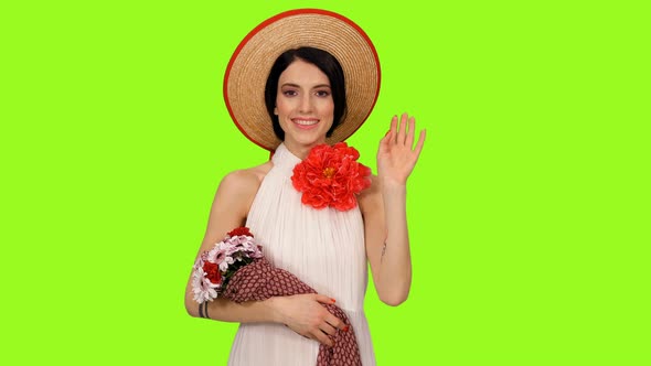 Charming Girl in Straw Hat and White Dress Standing with Bouquet and Waving Hi
