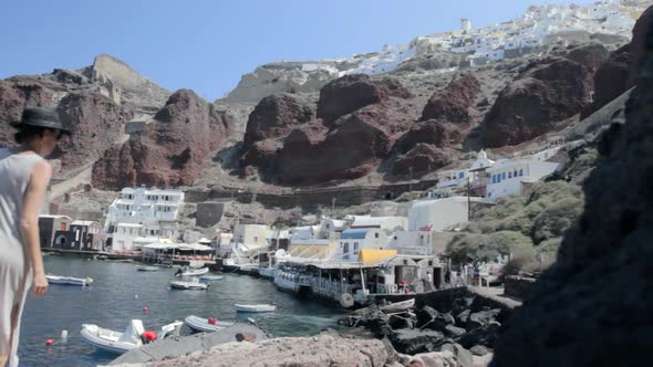 View of a small fishing harbor on a Greek island with a woman that strolls by the rocks. alt
