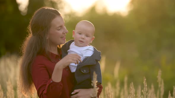 Happy family. Loving tender mum in a dress with a cute little baby on a field at sunset on a summer