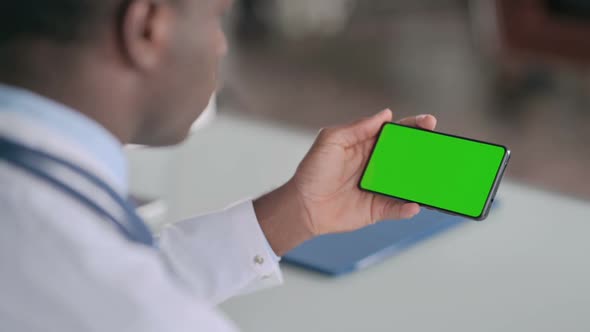 Rear View of African Doctor Holding Smartphone with Green Chroma Key Screen alt