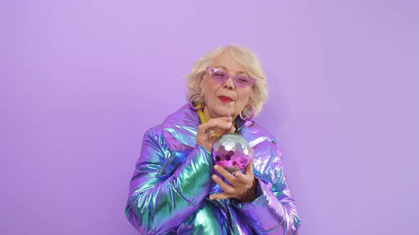 Charming Woman of Retirement Age Posing Standing on an Isolated Background Holding a Cocktail alt