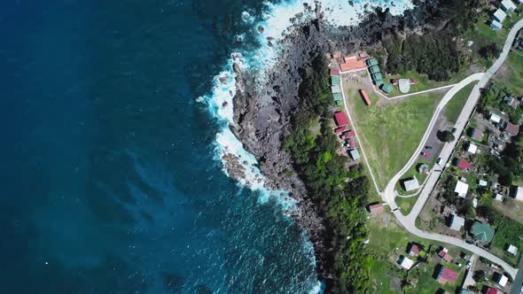 Overhead drone shot of azure sea, black coast and rooftops on the coast in Saint Kitts and Nevis alt