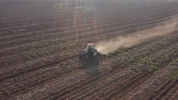 Red tractor flattening a field for seeding, Drone follow footage. alt