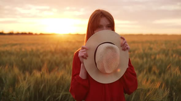 Slow Motion of Romantic Cute Redhead Girl in Red Dress Hiding Face Behind Straw Hat and Peeking with