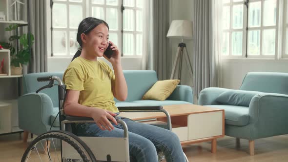 Asian Kid Girl Sitting In A Wheelchair And Talking On Phone At Home alt