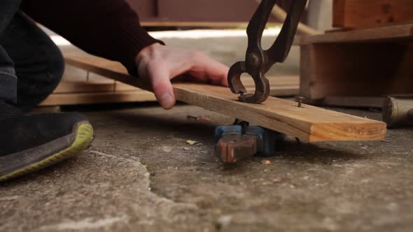 A Man Pulls Nails Out of a Wooden Board