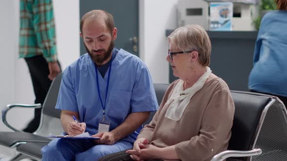 Male Nurse Consulting Senior Patient in Waiting Room at Medical Facility alt