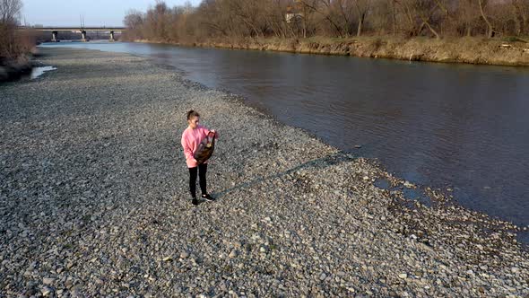Young woman with her son collects plastic garbage in a garbage bag on the river alt