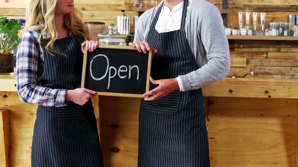Smiling waiter and waitresses holding open sign board alt