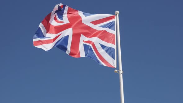Slow motion of national Great Britain symbol Union Jack waving on flag-pole against blue sky 1080p H alt