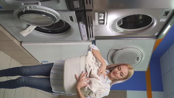 An Attractive Woman Loads Dirty Laundry Into the Washing Machine in the Laundry Room