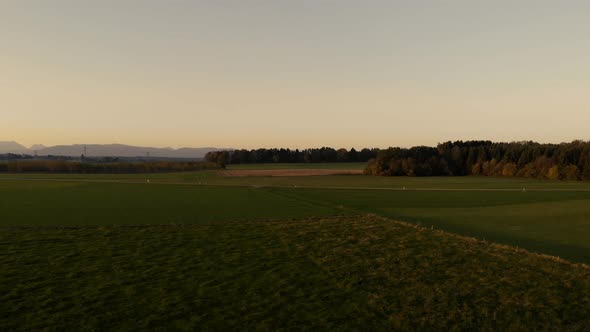 Tracking left over fields with a forest and the mountains in the background, aerial view. alt