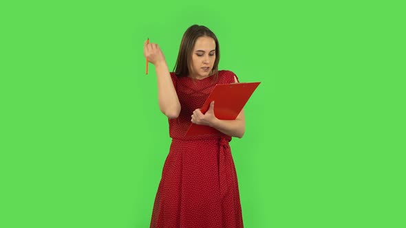 Tender Girl in Red Dress Fills Papers in Red Folder with Pensil. Green Screen alt
