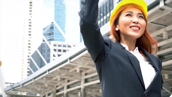 Young Asian Smart Engineer Looking Up the Sky with Success Gesture Over Building Cityscape alt