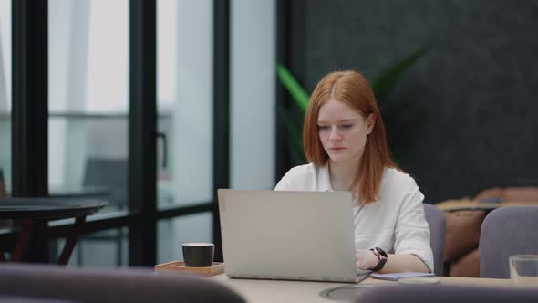 A Young Redhaired Woman is Working on a Laptop alt