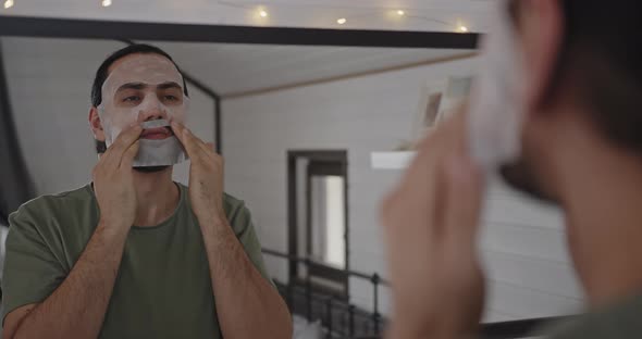 Closeup of a Young Man Face in Front of a Mirror Wearing a Cosmetic Sheet Mask