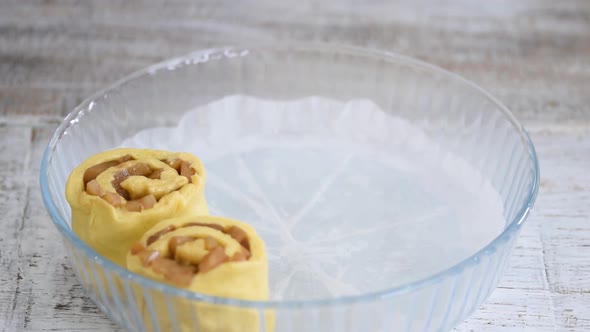 Baker put pear roll buns into glass baking form. Woman makes a yeast sweet roll buns. alt