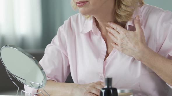 Unsatisfied Woman in Her 50s Looking Into a Hand Mirror, Anti-Age Cosmetics alt
