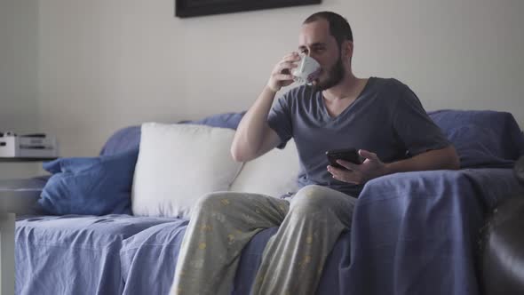 Man having his first coffee in the morning on the couch before working at home. alt
