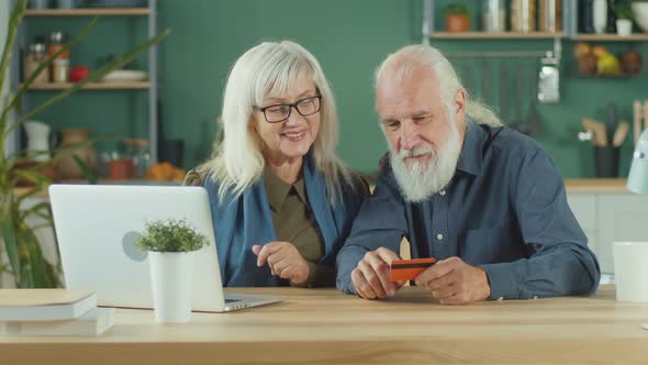 Happy Elderly Couple Shopping Online From Home Using Computer and Credit Card alt