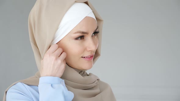 Muslim Woman Wearing Hijab Is Putting Wireless Earphone in Her Ear and Speaking Phone Using Headset alt