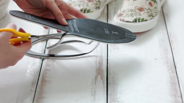 Woman's hands hold orthopedic insoles for shoes, comparing them with each other alt