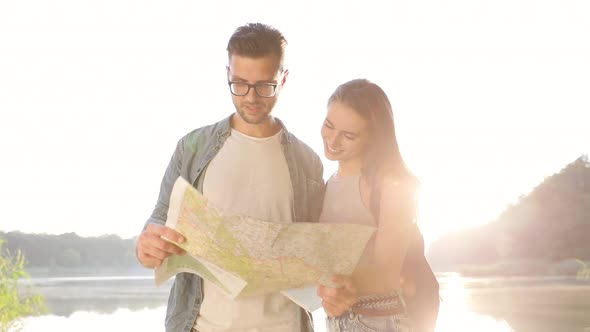 Close up view of Young Couple Hikers in the Wood. Standing by the Lake. Using Tourist Map. alt