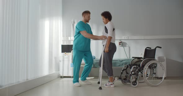 Male Medical Nurse Assisting African Young Woman Walking with Crutches alt