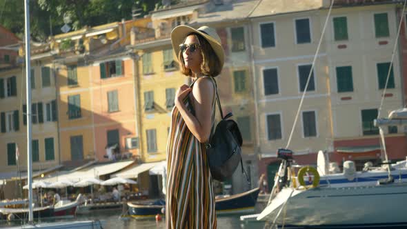 A woman walking wearing hat and backpack purse traveling, Portofino, Italy, luxury resort, Europe alt