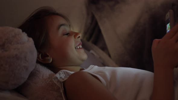 Little girl in bed playing games on the phone at night instead of sleeping.
