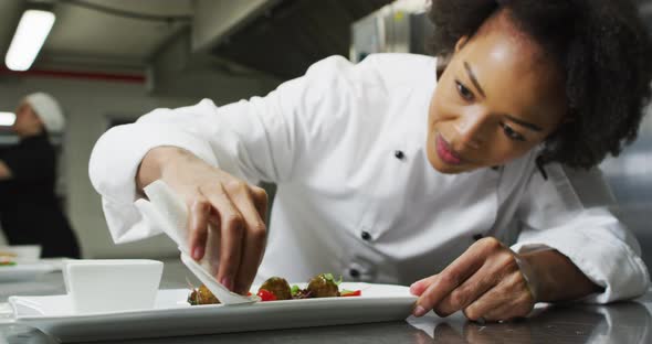 Portrait of african american female chef garnishing dish looking at camera and similing alt