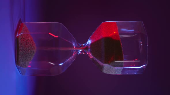 Glass Hourglass with Golden Sand on Purple Background alt