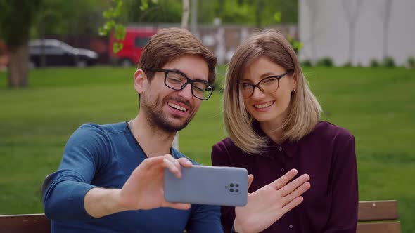Happy couple wearing eye glasses waving hands at camera during video chat. alt