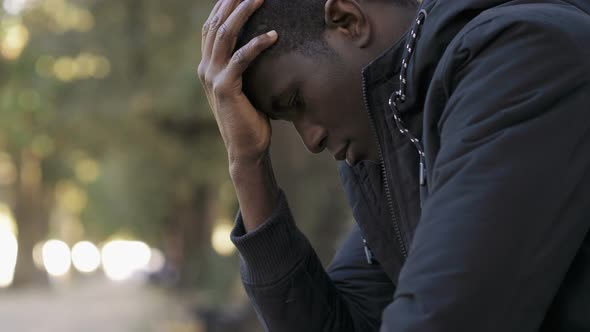 Desperate depressed young african man thinking alone in the park alt