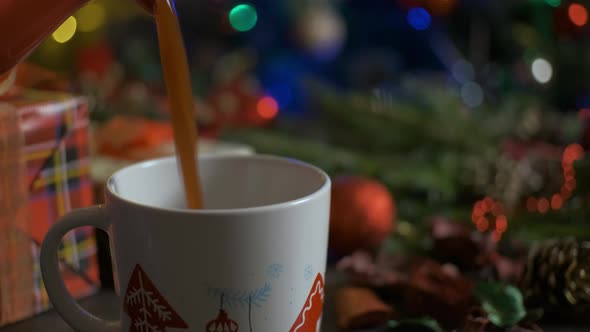 Close-up, Hot Cocoa Pouring Into a Cup on Background of Glowing Garland Lights. alt