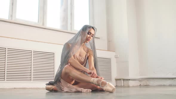 Ballerina in Stage Long Flowing Dress Sits on the Floor and Corrects Shoes