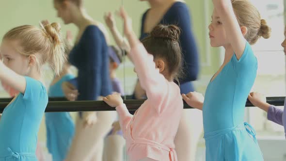 Female Ballet Dancer strides along the barre in the backgound encouraging the four young Ballerinas 