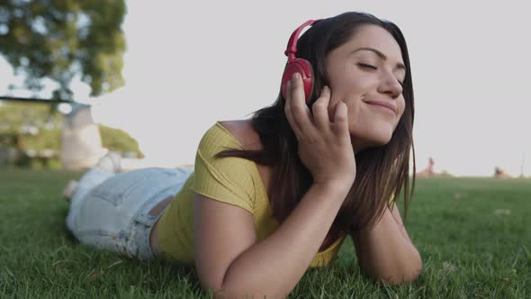 Young Hispanic Woman Listening to Music with Headphones While Relaxing on Green Grass at Park alt