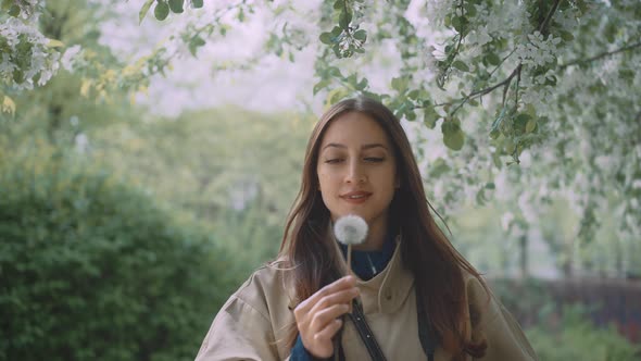 Young female blowing into dandelion while looking into the camera alt