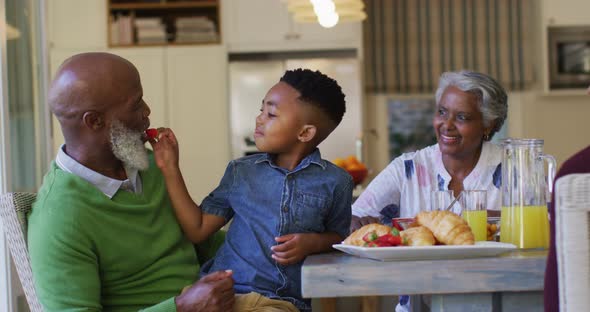 African american boy feeding strawberries to his grandfather while sitting on his lap at home alt