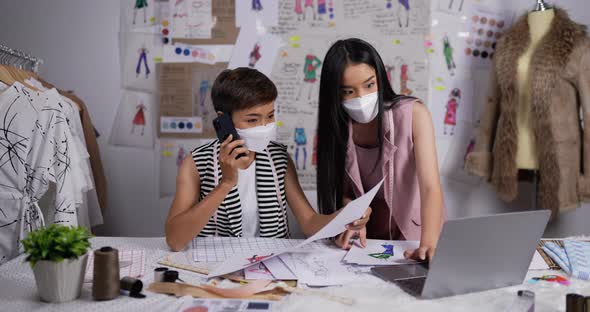 Two fashion designer woman looking a sketch of woman's clothing on laptop and talking alt