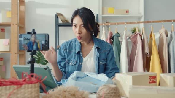 Asia lady designer using mobile phone receiving purchase order and show clothes recording video.
