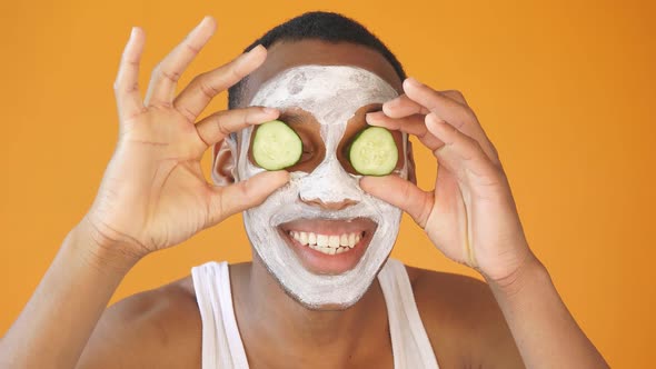 Positive African American Applies a White Face Mask with Cucumber Slices Expresses Positive Emotions