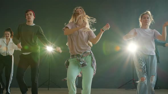 Team of Young Dancers Performing Creative Show on Stage with Lights in Background alt