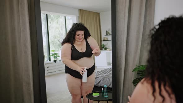 Young Overweight Woman Puts Cream on Arm Against Mirror alt