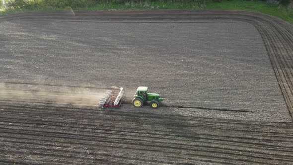 Farm field being prepared with perfectly straight rows. Clouds of dusty following the tractor.