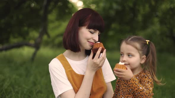 Beautiful Mom and Her Daughter Holding Tasty Cakes While Resting at Picnic at the Park alt