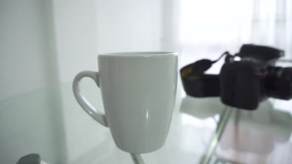 A cup of coffee and a camera on the table, waiting for the person who goes for them alt