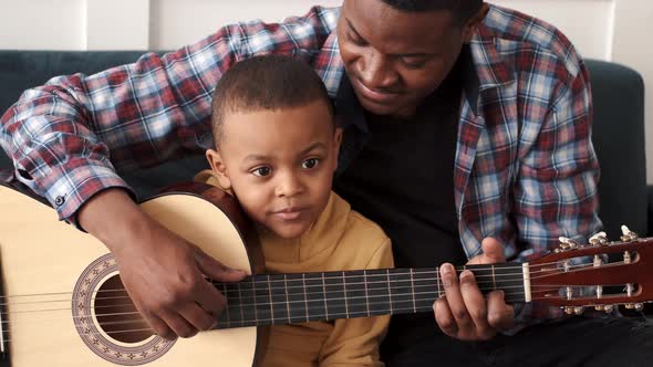 AfricanAmerican Man Teaching His Little Son to Play Guitar at Home alt
