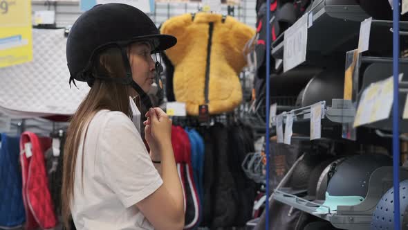 Young Woman is Buying a Riding Helmet in Sports Store alt